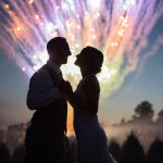 newlyweds silhouetted by fireworks behind them