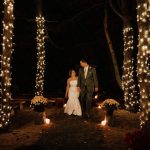 married couple laughing under a canopy of trees lit with white lights